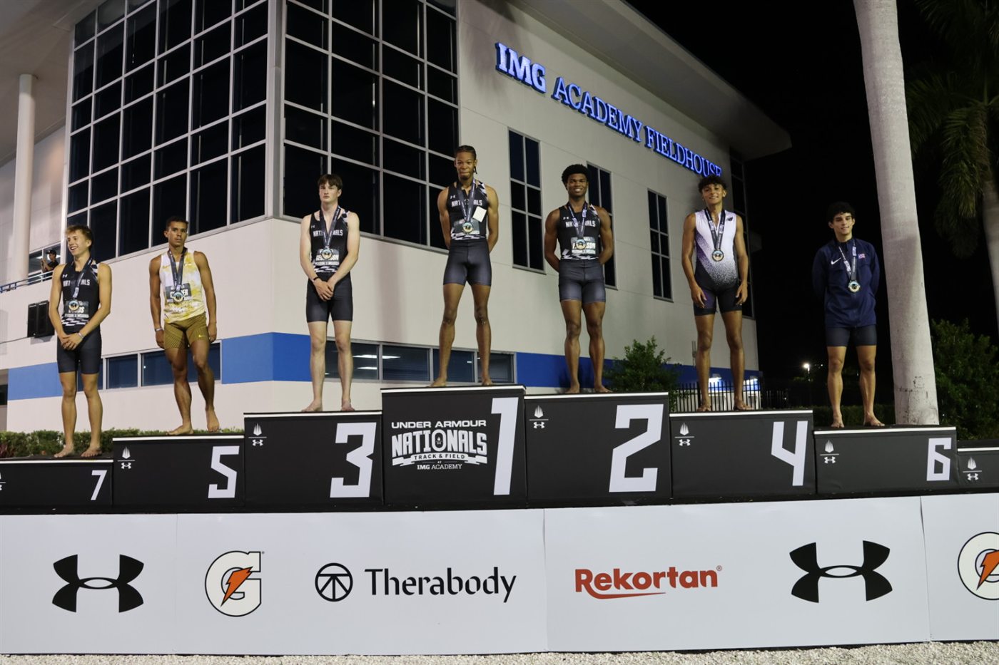 All seven finalists on the 2026 Under Armour Track & Field Nationals boys 800m podium in front of the IMG Academy Fieldhouse in Bradenton, Florida, with All-American Nicholas L. Ferguson of Houston Heights on the No. 2 step